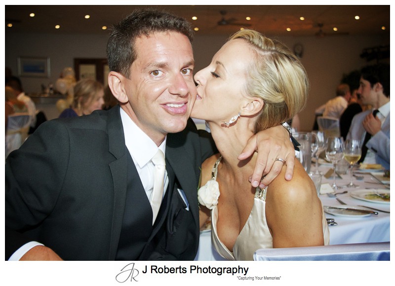 Bride kissing grooms cheek at wedding reception - wedding photography sydney
