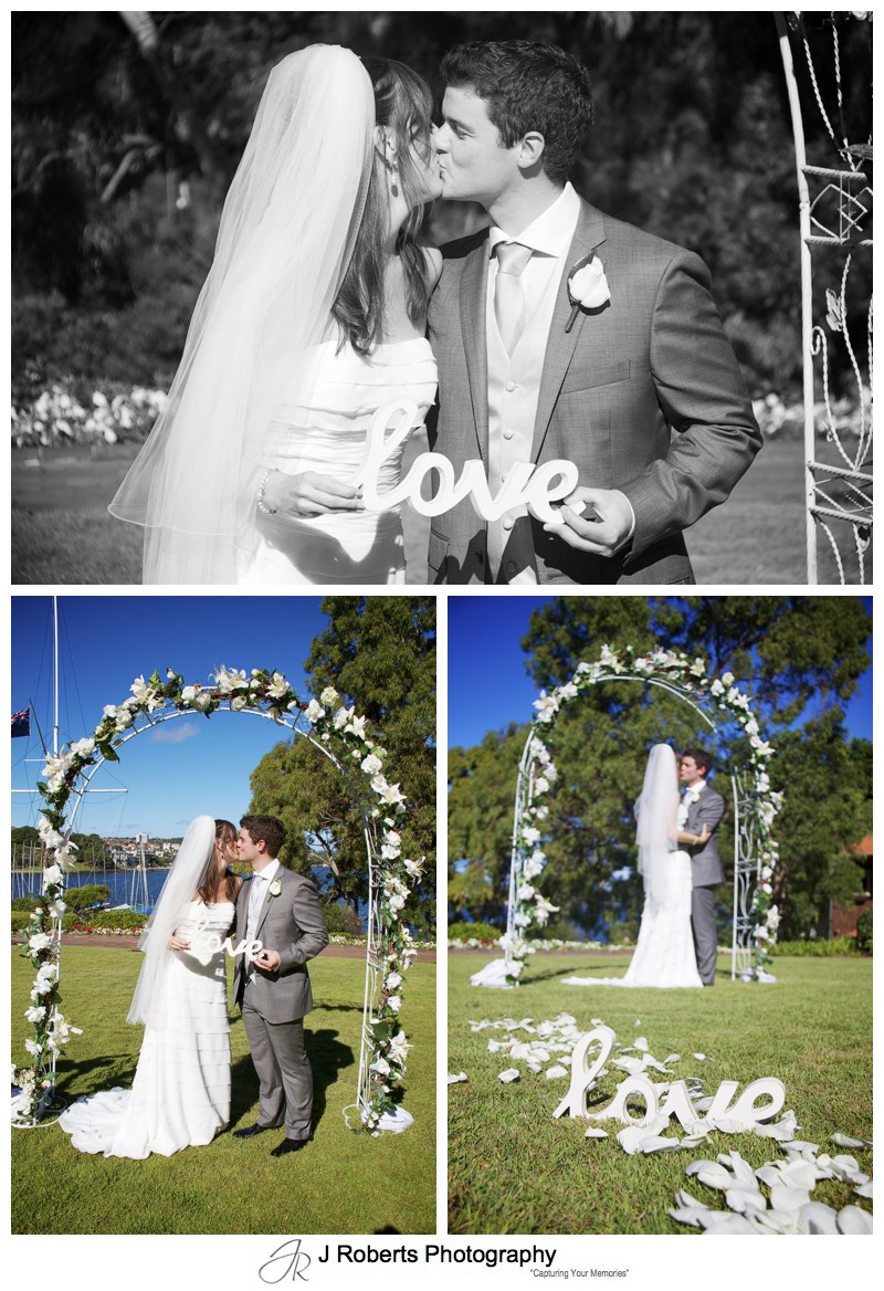 Bride and groom kissing under an flower arch with love sign - wedding photography sydney